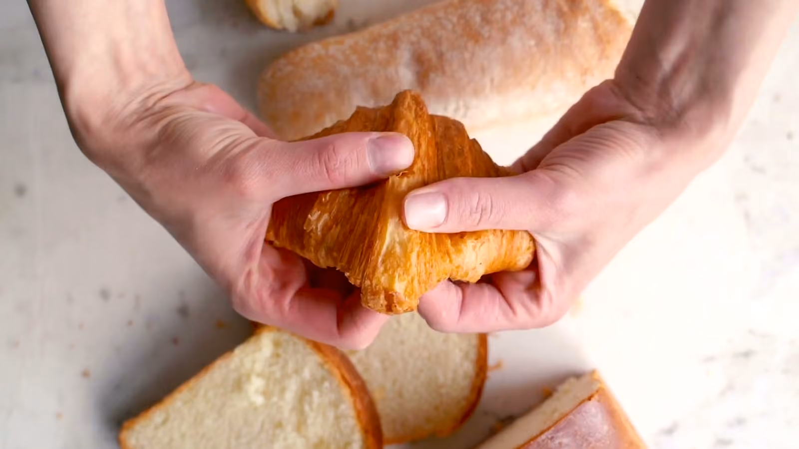 Hands gently tear a golden croissant, revealing its crumb