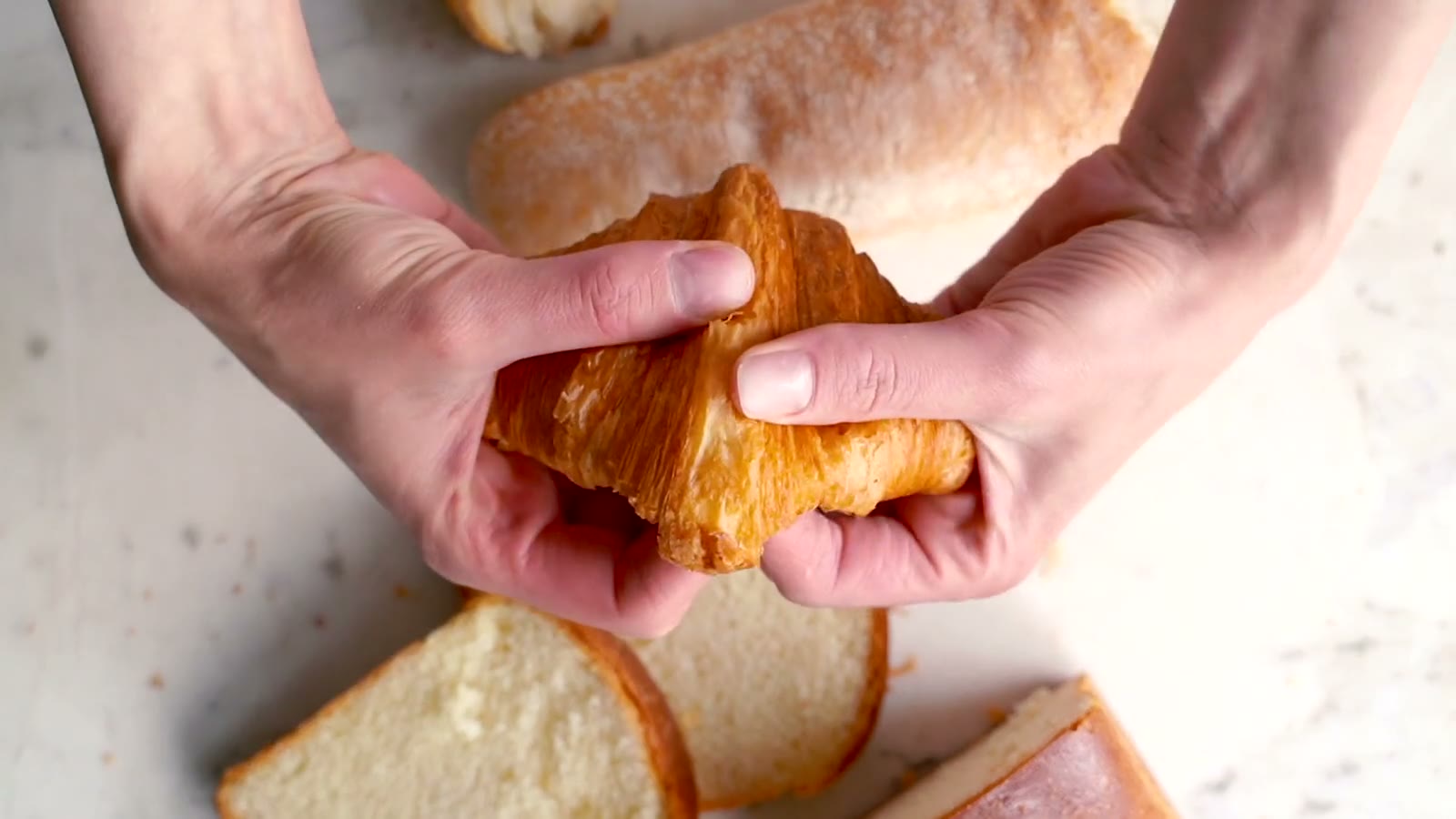 Hands gently tear a golden croissant, revealing its crumb